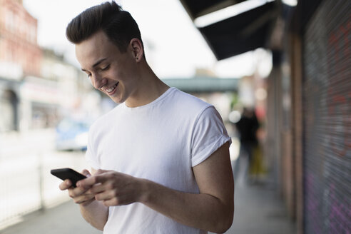 Lächelnder Teenager, der ein Smartphone auf einem Bürgersteig benutzt - CAIF22430