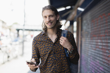 Porträt selbstbewusster Hipster-Mann mit Smartphone auf städtischem Bürgersteig - CAIF22433