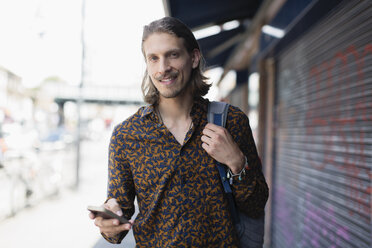 Portrait confident hipster man with smart phone on urban sidewalk - CAIF22433