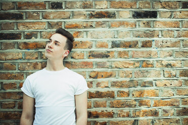 Thoughtful teenage boy standing at brick wall - CAIF22434