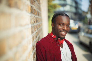 Porträt eines lächelnden, selbstbewussten Teenagers mit Kopfhörern auf einem städtischen Bürgersteig - CAIF22445