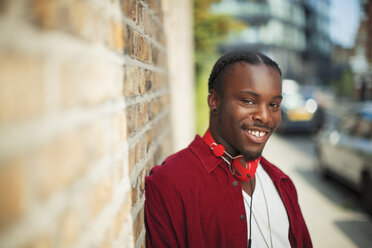 Portrait smiling, confident teenage boy with headphones on urban sidewalk - CAIF22445