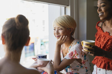 Junge Freundinnen trinken Kaffee am Wohnungsfenster - CAIF22465