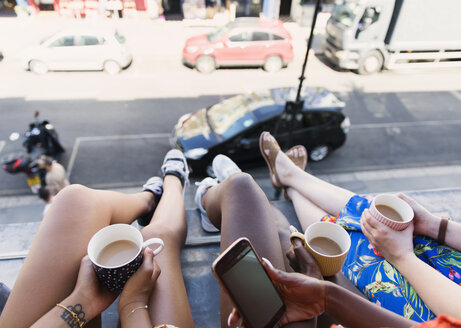 Freundinnen, die Kaffee trinken und die Beine aus dem Fenster einer städtischen Wohnung baumeln lassen - CAIF22473