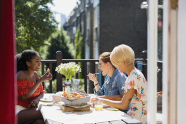 Young women friends eating brunch on sunny apartment balcony - CAIF22480