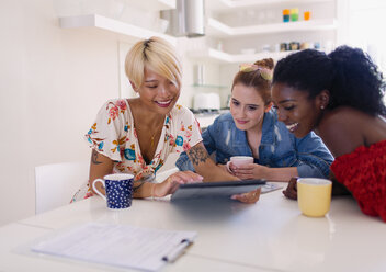 Young women friends drinking coffee and using digital tablet at kitchen table - CAIF22483