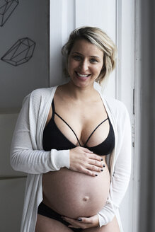 Porträt einer lächelnden blonden schwangeren Frau zu Hause - IGGF00725