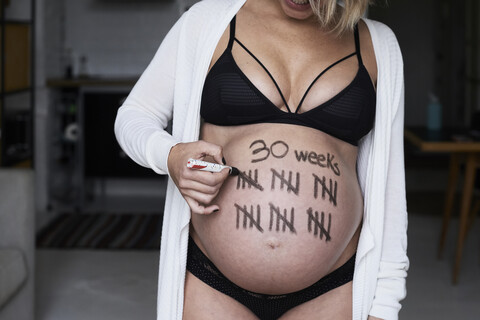 Nahaufnahme einer schwangeren Frau, die Strichmännchen auf ihren Bauch malt, lizenzfreies Stockfoto