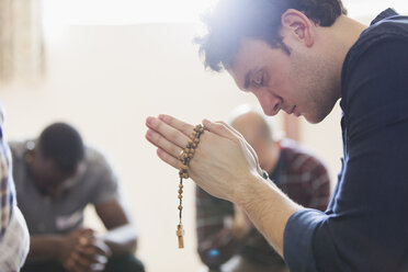 Gelassener Mann betet mit Rosenkranz in Gebetsgruppe - CAIF22507