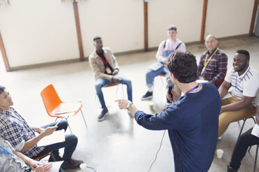 Mann mit Mikrofon im Gespräch mit Männern in einer Gruppentherapie - CAIF22509