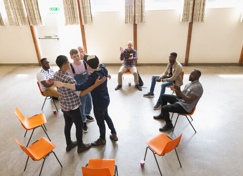 Männer, die sich in der Gruppentherapie umarmen und klatschen, lizenzfreies Stockfoto