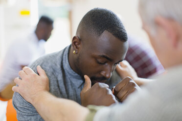 Mann tröstet jungen Mann in Gruppentherapie - CAIF22547