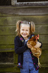 Lächelndes Mädchen hält ein Huhn und schaut in die Kamera. - MINF09830
