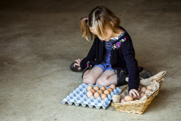 Mädchen kniet auf dem Boden und legt Eier in einen Korb. - MINF09835
