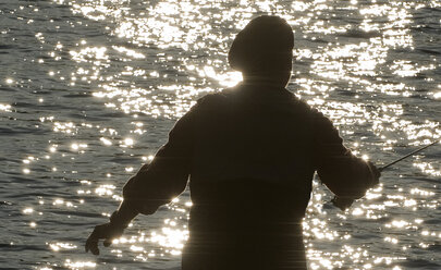 Silhouette eines Fliegenfischers, der an einem Fluss nach Forellen wirft - MINF09875