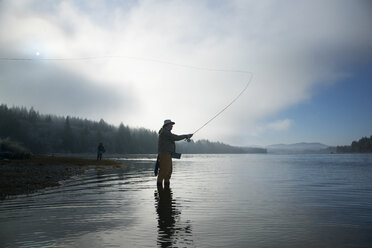 Silhouette of fisherman fly fishing for salmon and sea run cutthroat trout - MINF09876