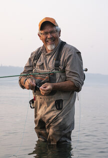 Caucasian senior male tying a fly on his fly fishing line while fishing for  salmon and