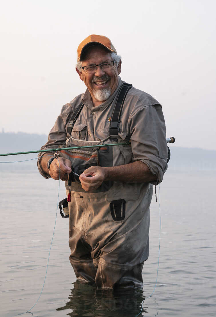 Caucasian senior male tying a fly on his fly fishing line while fishing for  salmon and searun cutthroat trout stock photo