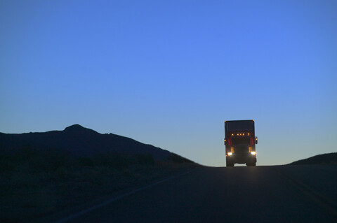 Ein Lastwagen der Klasse 8, der auf der Autobahn über eine Anhöhe fährt, wird als Silhouette dargestellt., lizenzfreies Stockfoto