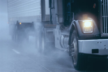 Teilansicht eines großen Lastkraftwagens, der unter gefährlichen Bedingungen bei Schnee und Regen auf einer Autobahn fährt. - MINF09943