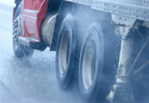 Teilansicht eines großen Lastkraftwagens, der unter gefährlichen Bedingungen bei Schnee und Regen auf einer Autobahn fährt., lizenzfreies Stockfoto