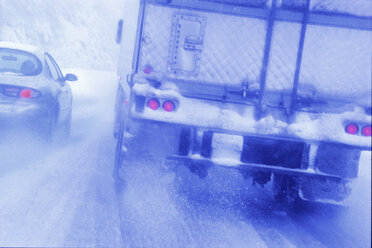 Teilansicht eines großen Lastkraftwagens, der unter gefährlichen Bedingungen bei Schnee und Regen auf einer Autobahn fährt. - MINF09946