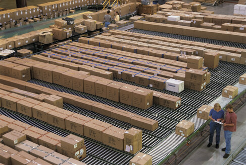 Overview of a large industrial distribution warehouse storing products in cardboard boxes on conveyor belts and racks. - MINF09954