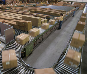 Überblick über ein großes industrielles Auslieferungslager, in dem Produkte in Kartons auf Förderbändern und Regalen gelagert werden. - MINF09956