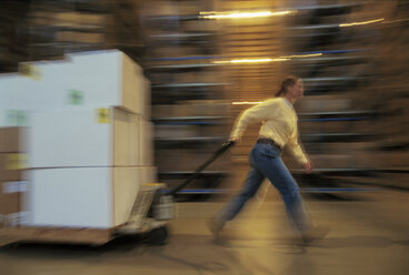 Ein Lagermitarbeiter bewegt eine Palette mit Produkten in Kartons in einem großen Vertriebslager. - MINF09957
