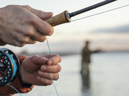Nahaufnahme der Hände eines Fliegenfischers, der seine Fliegenrute und die Schnur beim Fischen hält. - MINF10050