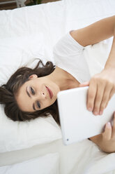 Young woman lying on bed, using digital tablet, reading - BSZF00808