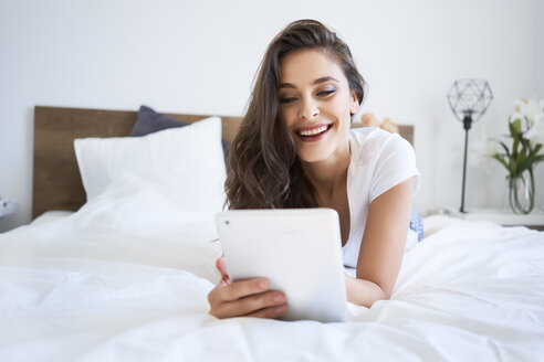 Junge Frau auf dem Bett liegend, mit digitalem Tablet, lesend - BSZF00816
