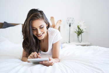 Junge Frau auf dem Bett liegend, mit digitalem Tablet, lesend - BSZF00817