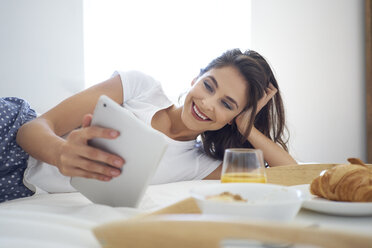 Junge Frau, die im Bett frühstückt, ein digitales Tablet benutzt und liest - BSZF00824
