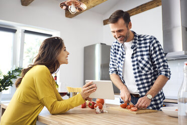 Affectionate couple in kitchen, preparing spaghetti toghether, using digital tablet - BSZF00854