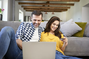 Couple sitting in living room, using laptop, making an online payment with their credit card - BSZF00868