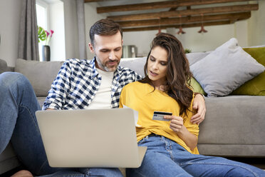 Couple sitting in living room, using laptop, making an online payment with their credit card - BSZF00869