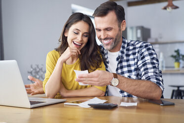 Couple sitting at dining table, using laptop, checking bills - BSZF00873