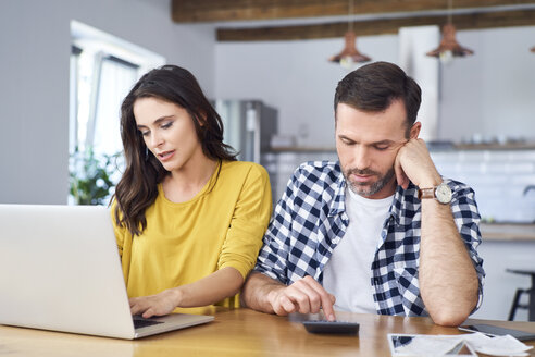 Ein besorgtes Paar sitzt am Esstisch, benutzt einen Laptop und prüft seine Finanzen - BSZF00874