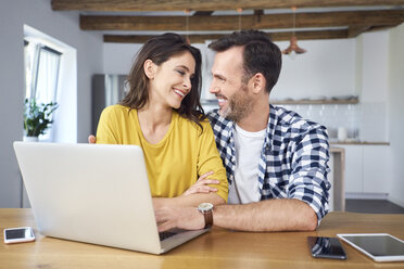 Ehepaar am Esstisch sitzend, mit Laptop, lächelnd - BSZF00877