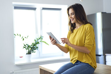 Frau sitzt zu Hause am Küchentisch und benutzt ein digitales Tablet - BSZF00884
