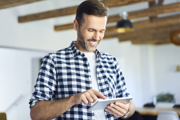 Man using tablet at home and smiling - BSZF00891