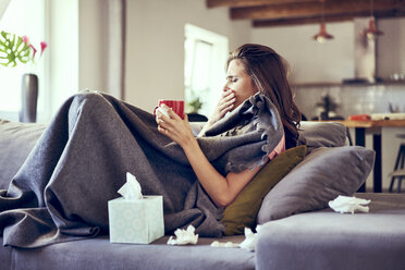 Porträt einer Frau, die krank auf dem Sofa liegt, hustet und versucht, heißen Tee zu trinken - BSZF00892