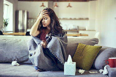 Portrait of sick woman sitting on couch and holding her aching head - BSZF00897