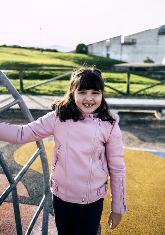 Porträt eines lächelnden Mädchens mit rosa Lederjacke auf einem Spielplatz, lizenzfreies Stockfoto