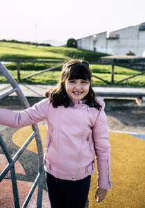 Porträt eines lächelnden Mädchens mit rosa Lederjacke auf einem Spielplatz - MGOF03927
