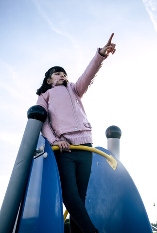 Mädchen in rosa Lederjacke auf einem Spielplatz, das auf etwas in der Ferne zeigt, lizenzfreies Stockfoto