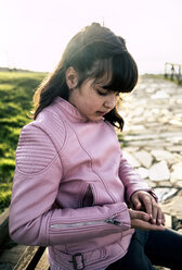 Mädchen in rosa Lederjacke betrachtet einen Kieselstein in ihrer Hand - MGOF03938