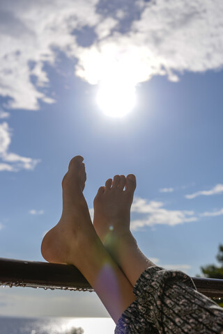 Füße eines Mädchens, das sich bei Gegenlicht an ein Geländer lehnt, lizenzfreies Stockfoto