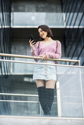Lächelnde junge Frau schaut auf ihr Handy - JSMF00724